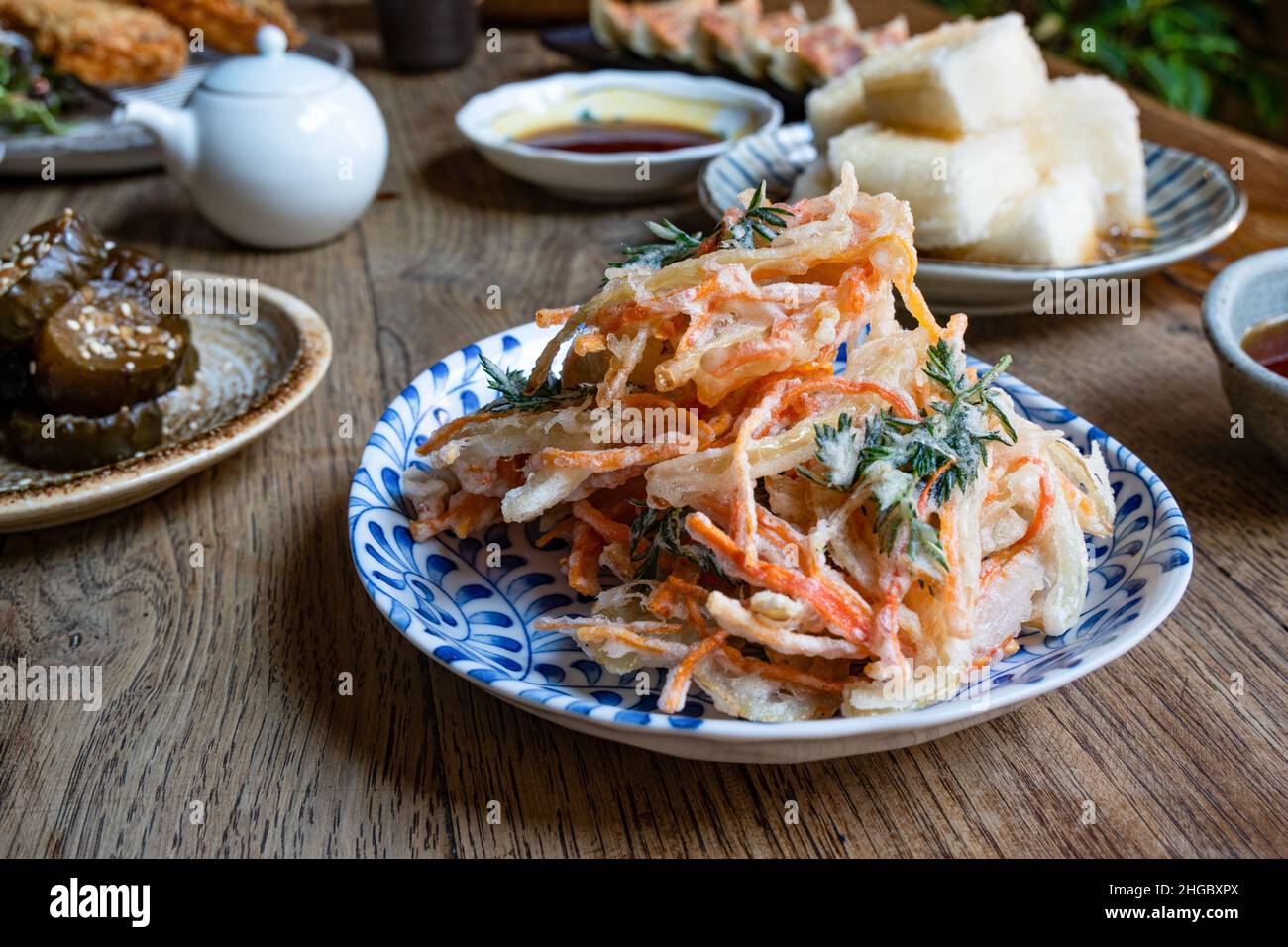 Tempura deep fried vegetables, with various Japanese dishes in the background. Wooden rustic table. Stock Photo