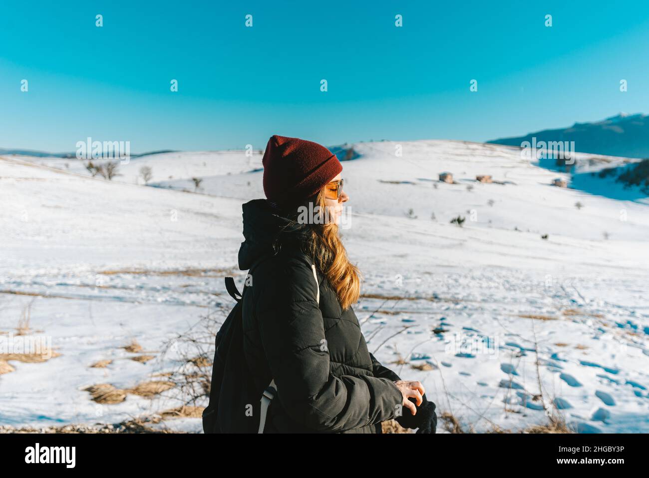 woman with hat and glasses enjoying the sun outdoors in mountains covered with snow Stock Photo