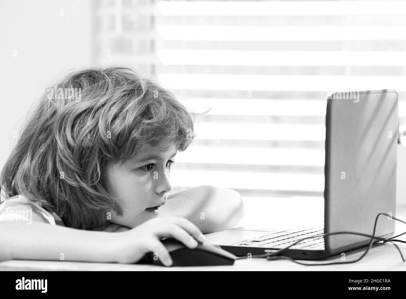 Smart little caucasian boy child sit at table study at laptop notebook, prepare homework at home
