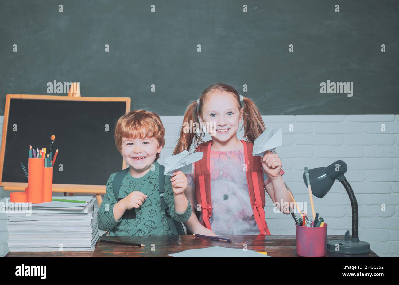 Back to school and happy time. Funny little child having fun on blackboard background. Friendly child in classroom play with paper airplane near Stock Photo