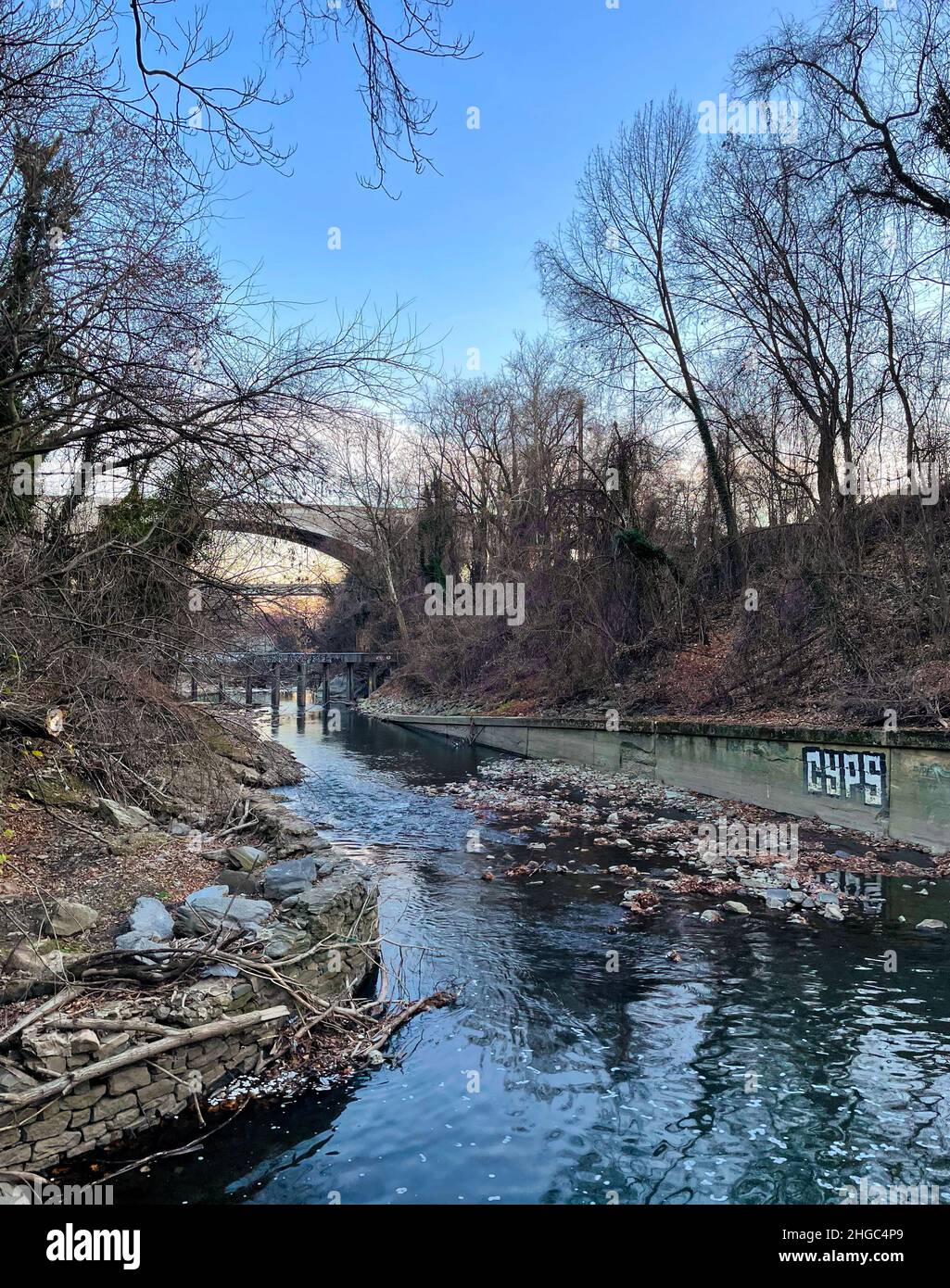 Brown leaves, bare trees, and grafitti surround the stone and wood walled Jones Falls late in the afternoon on a winter day in Baltimore, Maryland. Stock Photo