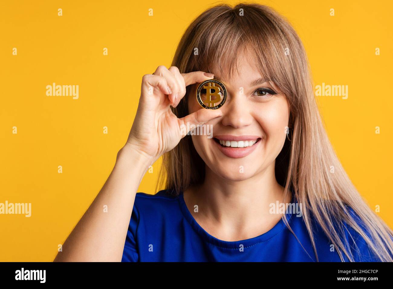 Smiling Girl in Blue Wear Holds Golden Physical Bitcoin in Front her Eye.  Closeup fun emotional female with Cryptocurrency Coin on Yellow Background.  Digital Currencies, Cryptocurrencies, Blockchain Stock Photo - Alamy