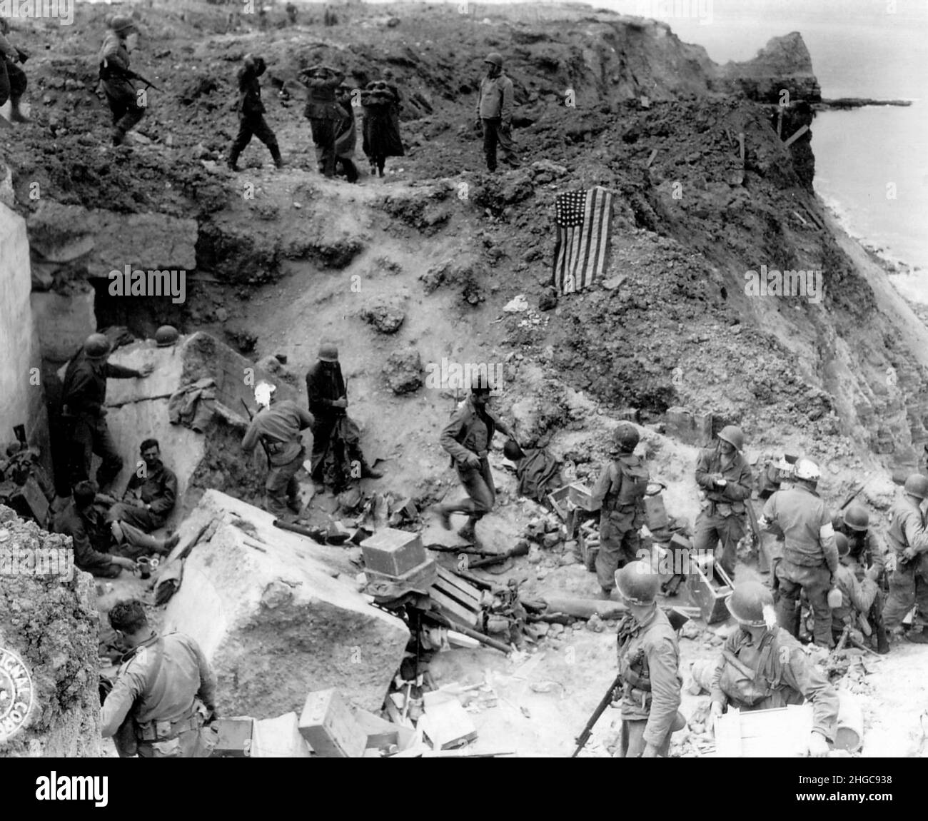 Two days after D-Day, after relief forces reached the Rangers on the cliffs of Pointe du Hoc. At the top of the image German soldiers can be seen surrendering. The American flag is put out to prevent friendly fire. Stock Photo