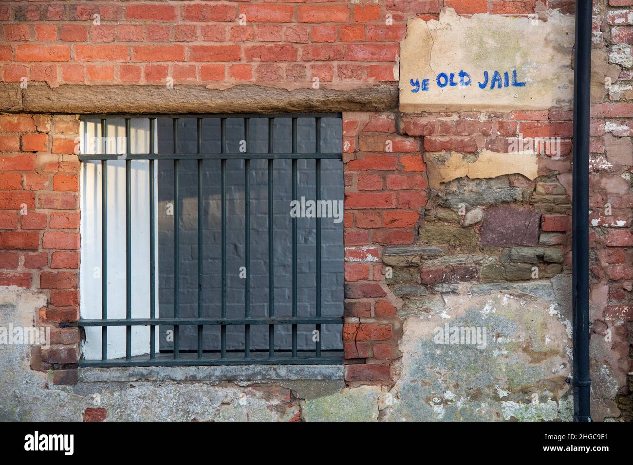Ye old jail graffiti next to a barred window in the side of an old brick wall. Castle square, Ludlow, Shropshire, England Stock Photo
