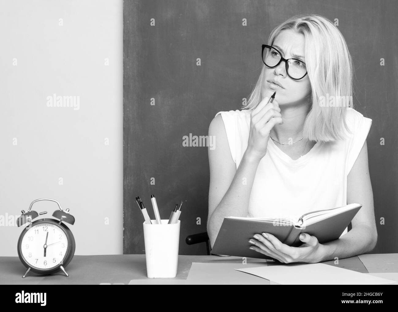 The teacher thinking in the classroom on blackboard background. Serious