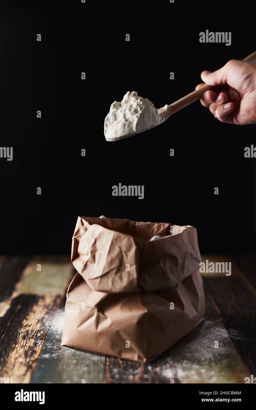 Wheat flour in a craft package. Freeze movement, spoon dark background, sprinkle flour. Front view. Stock Photo
