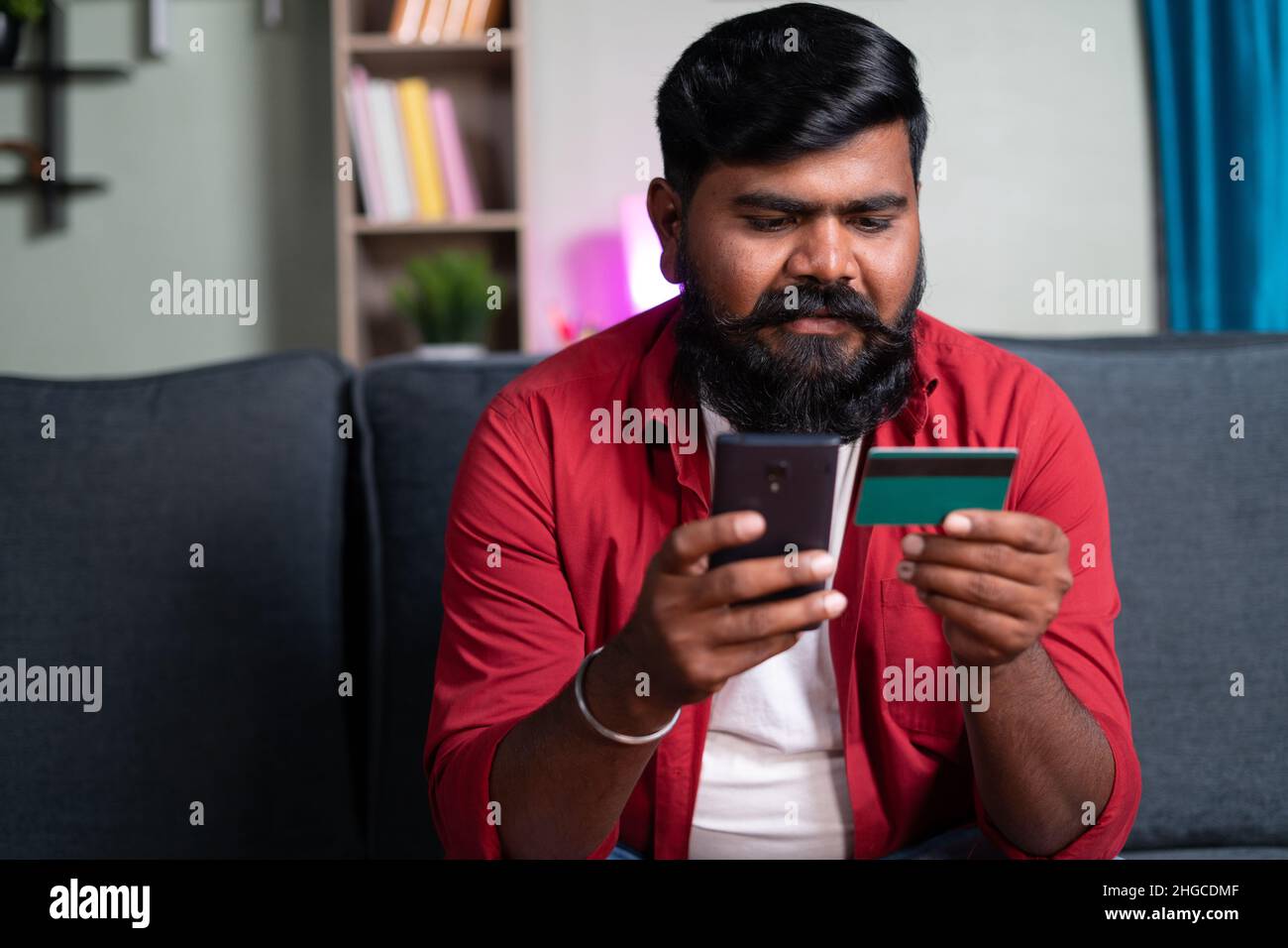 Young man with Beard making online payment using credit on mobile phone from home - concept of credit card debt paymnet, e-commerce purchase and Stock Photo