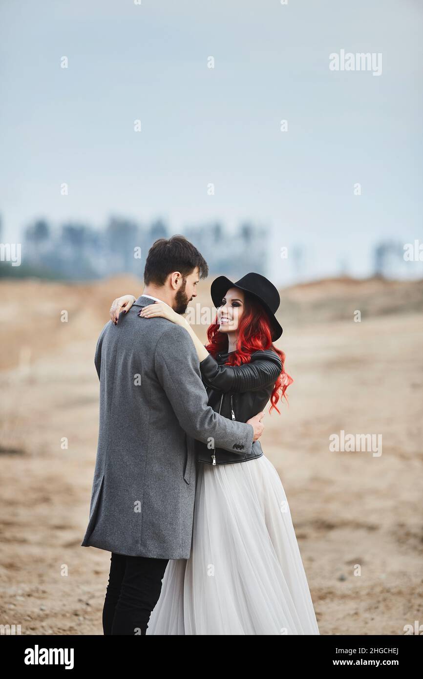 A fashionable couple of newlyweds posing outdoors. Stylish bearded man and  his red-haired girlfriend in a wedding dress and leather jacket Stock Photo  - Alamy