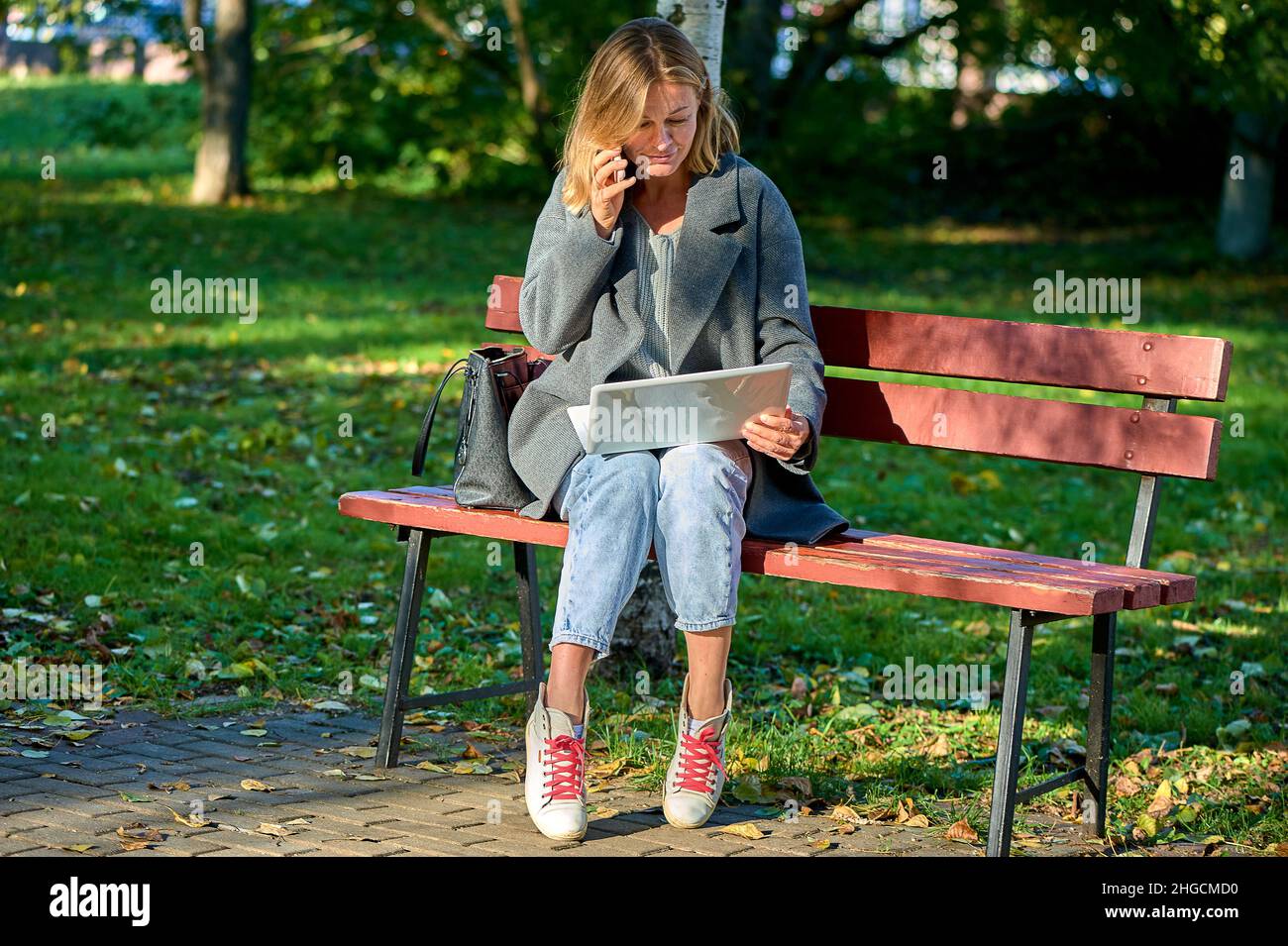 A woman with a laptop is sitting on a park bench on a sunny summer day Stock Photo