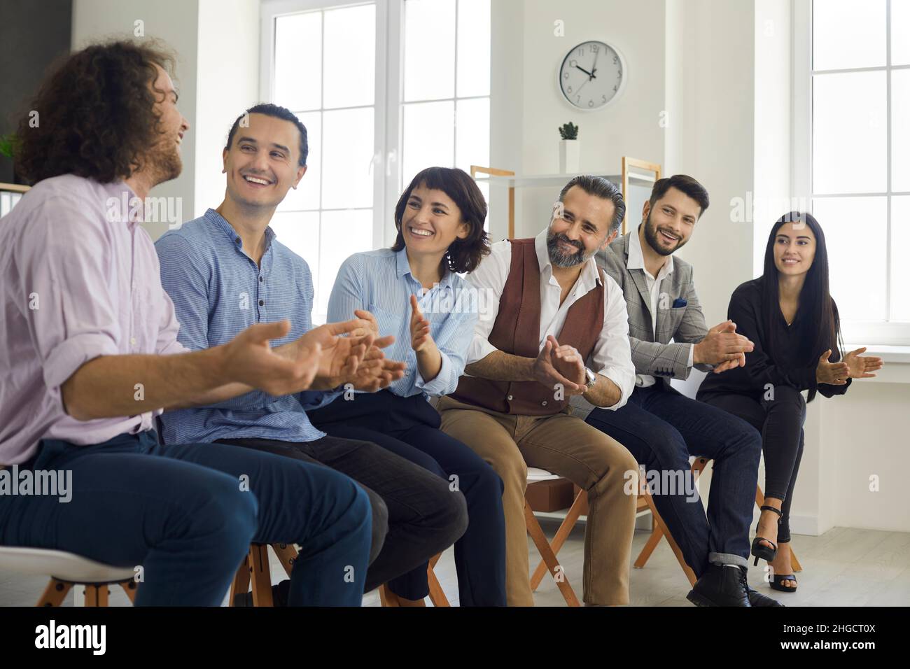 A group of young office colleagues at a seminar, smiling and applauding their male colleague for an emotional story. Stock Photo