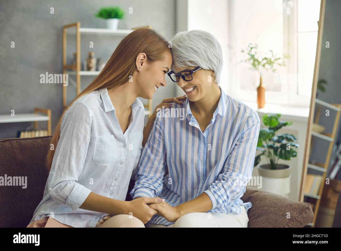 Happy loving senior mother and grown up daughter sitting on sofa, holding hands and smiling Stock Photo