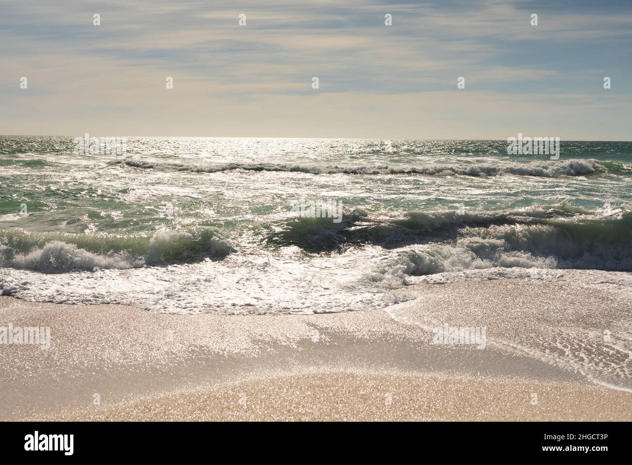 Scenic view of waves crashing on shore at beach against sky during sunny day Stock Photo