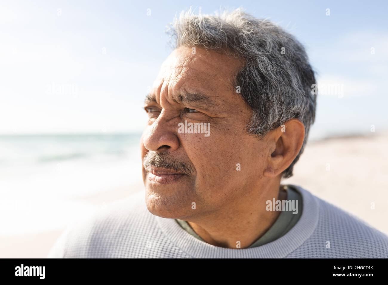 Close-up of retired biracial senior man looking away while thinking at beach during sunny day Stock Photo