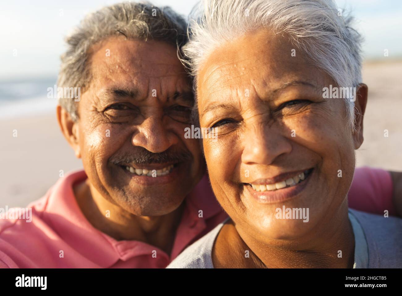 Close-up portrait of smiling multiracial senior couple with white hair enjoying sunset at beach Stock Photo
