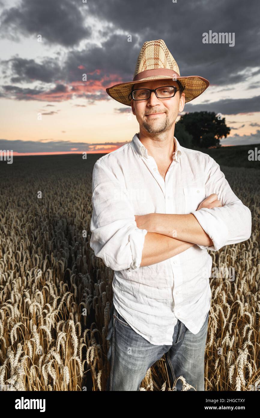 Farmer in a straw hat and glasses standing in a ripe wheat field before ...