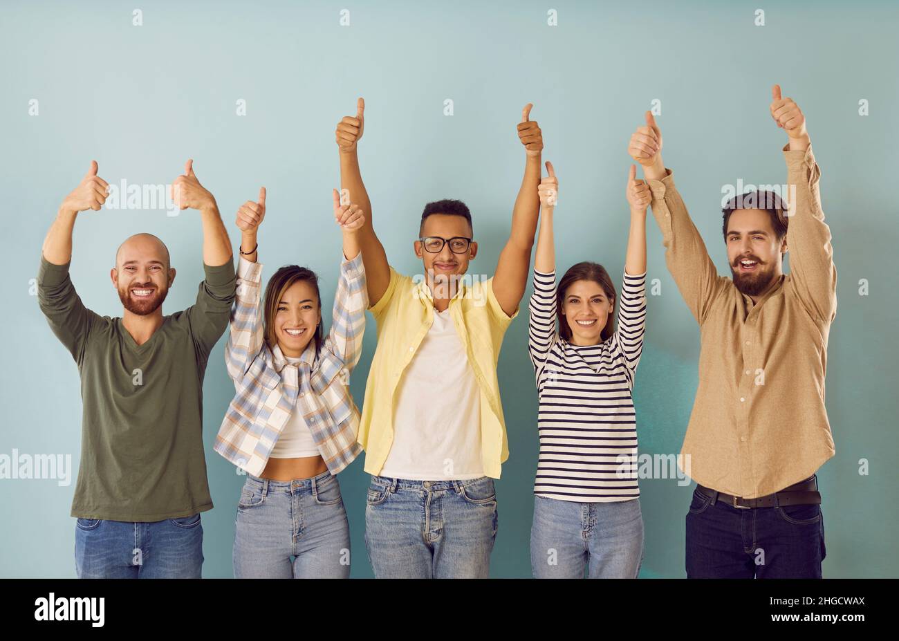 Young people make happy gesture by raising their hands with thumbs up demonstrating success. Stock Photo