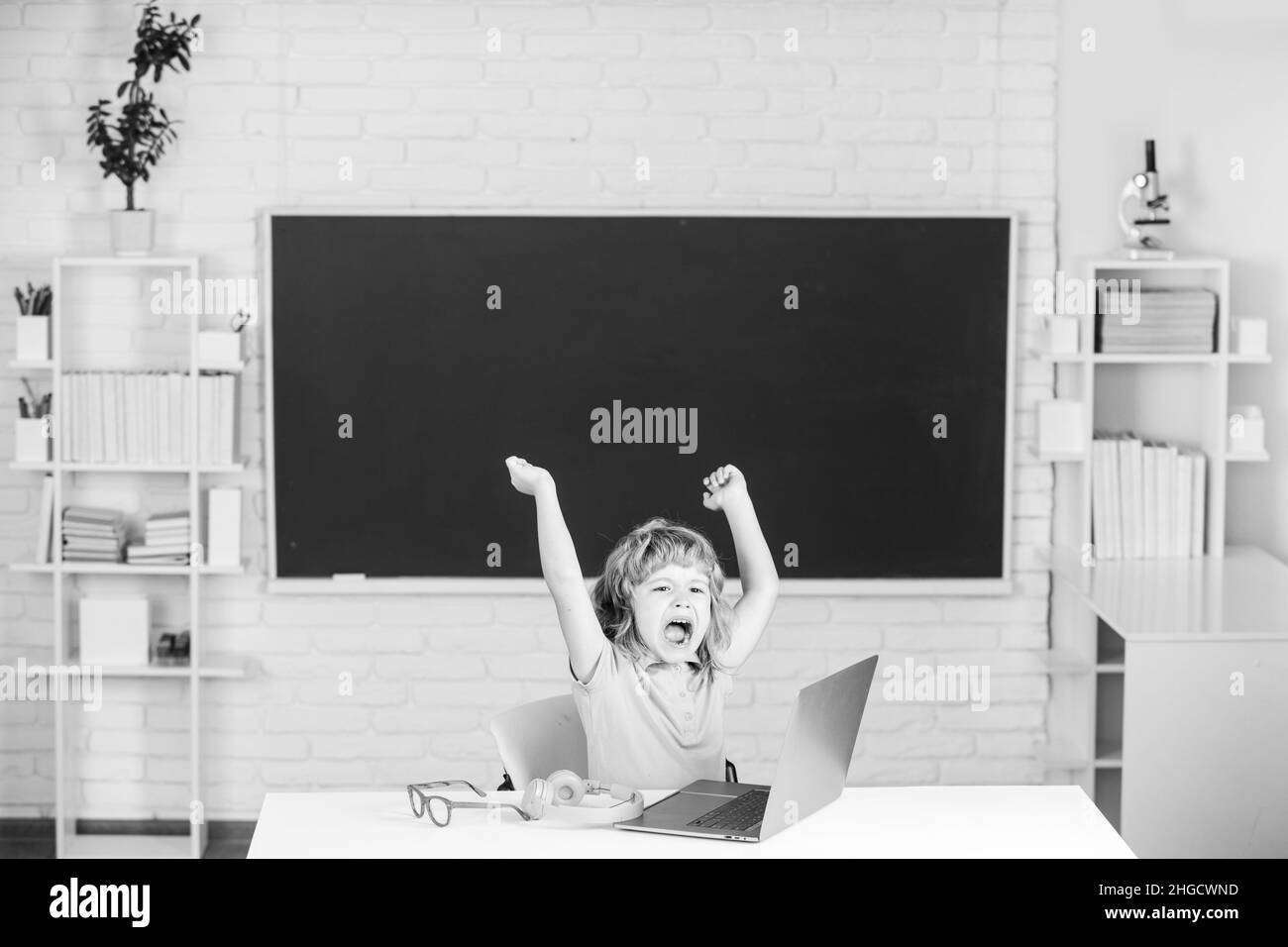 Angry sad screaming kid boy shouting on lesson at school, making homework and using notebook gadget. Bad school boy. Stock Photo