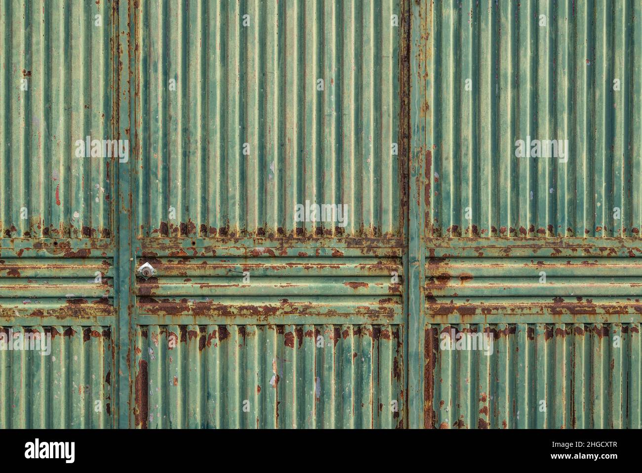 Industrial background texture, showing a weathered corrugated metal gate with rust and peeling green paint Stock Photo