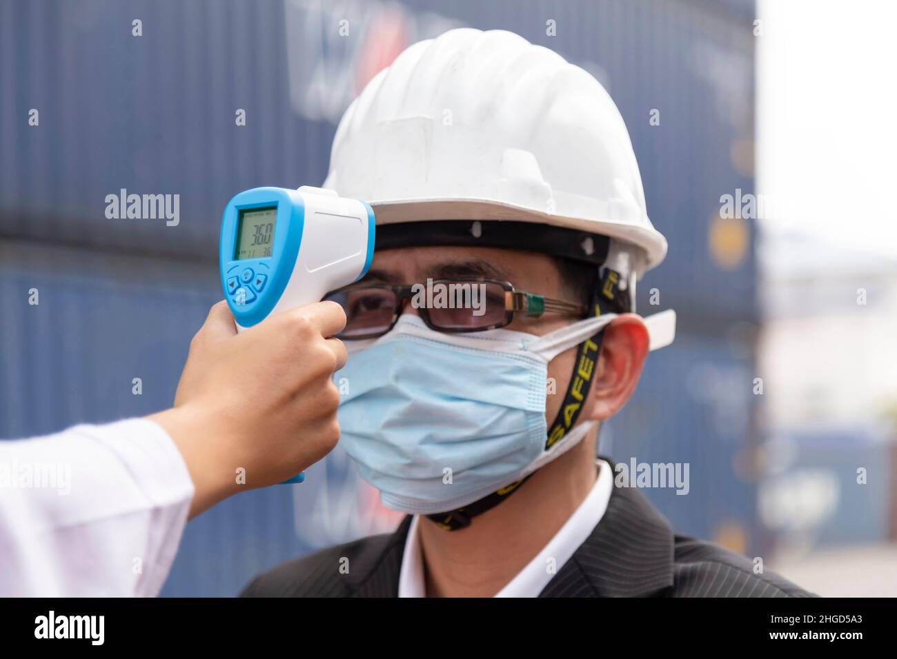 asian businessman wearing face mask checking fever by digital thermometer before entering to office meeting in construction site for protecting from c Stock Photo