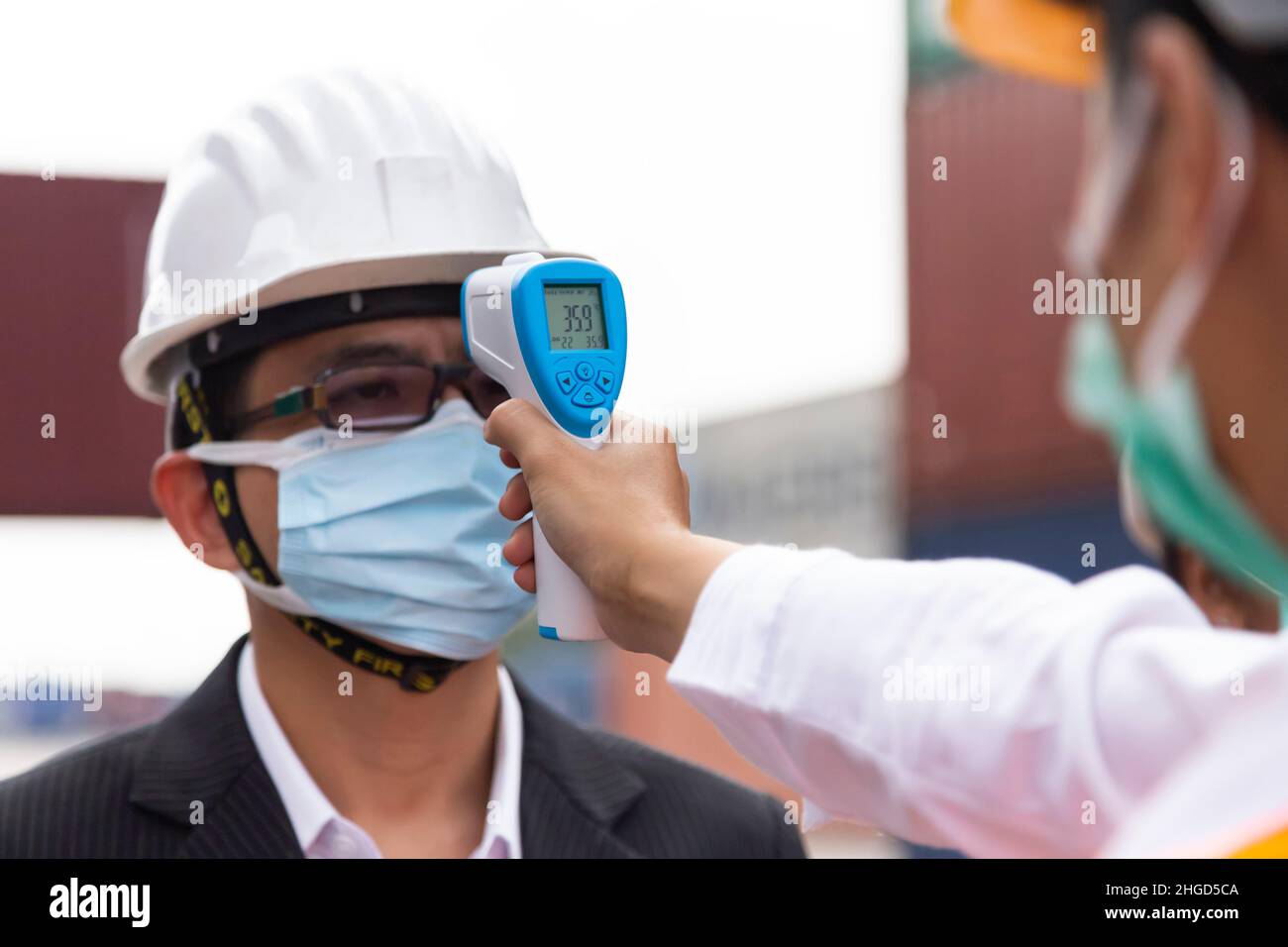 asian businessman wearing face mask checking fever by digital thermometer before entering to office meeting in construction site for protecting from c Stock Photo