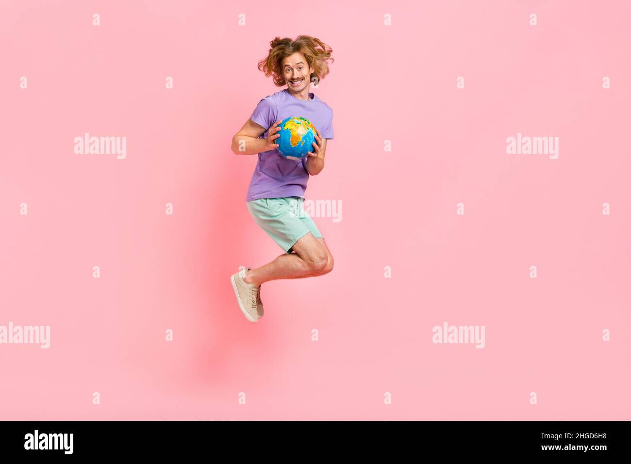 Full length body size view of attractive cheerful guy jumping holding in hands map globe isolated over pink pastel color background Stock Photo