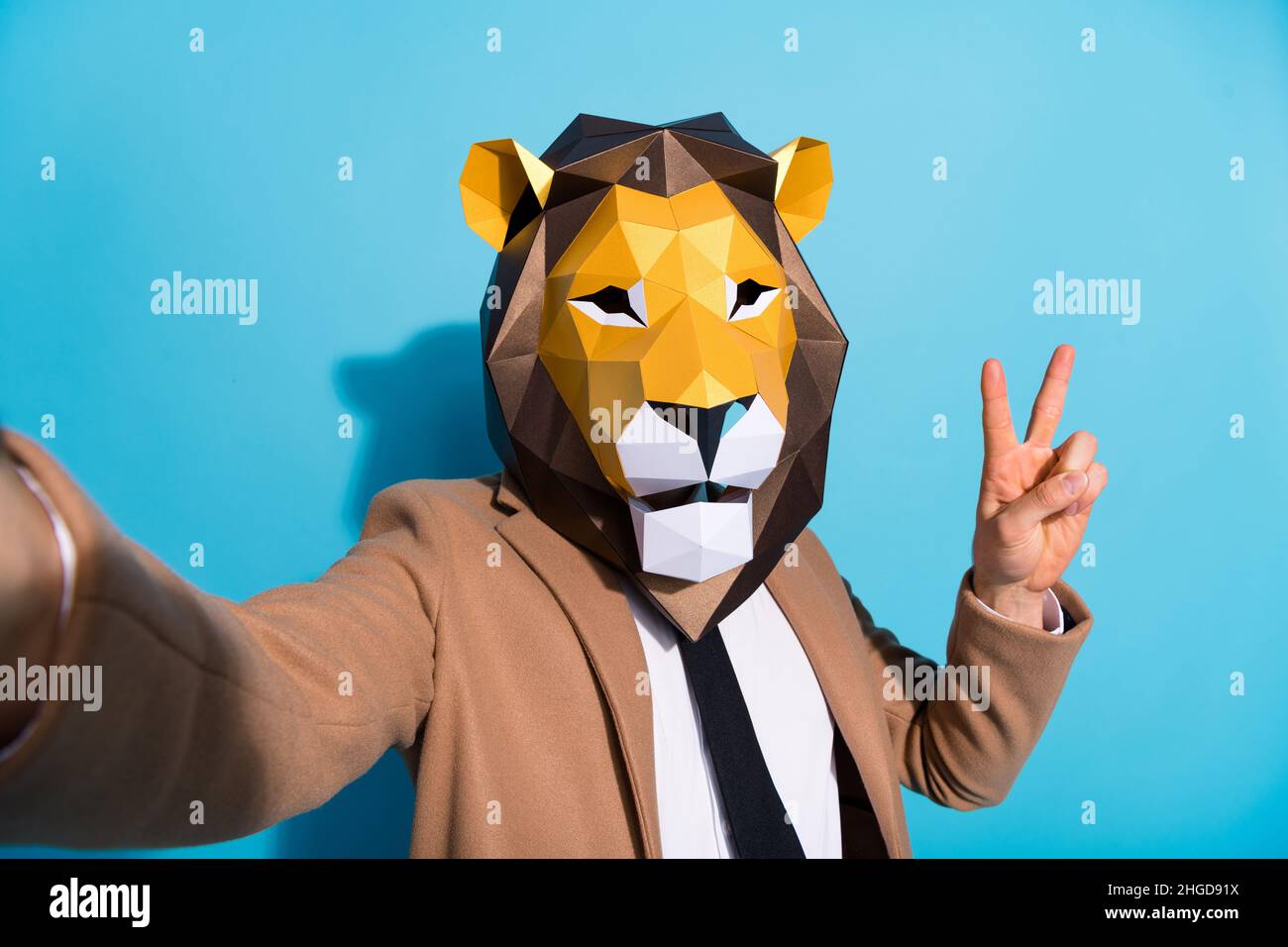 Portrait of weird incognito guy lion mask take selfie video call unusual occasion make v-sign isolated over blue color background Stock Photo