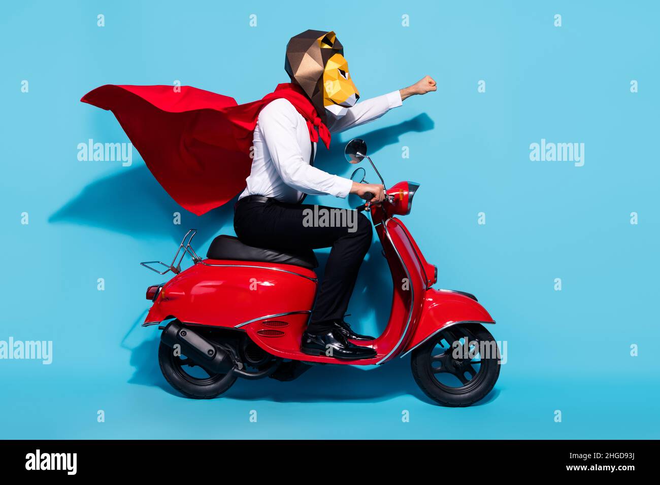Full body profile side photo of weird lion mask wear red mantle guy ride scooter protect planet isolated over blue color background Stock Photo