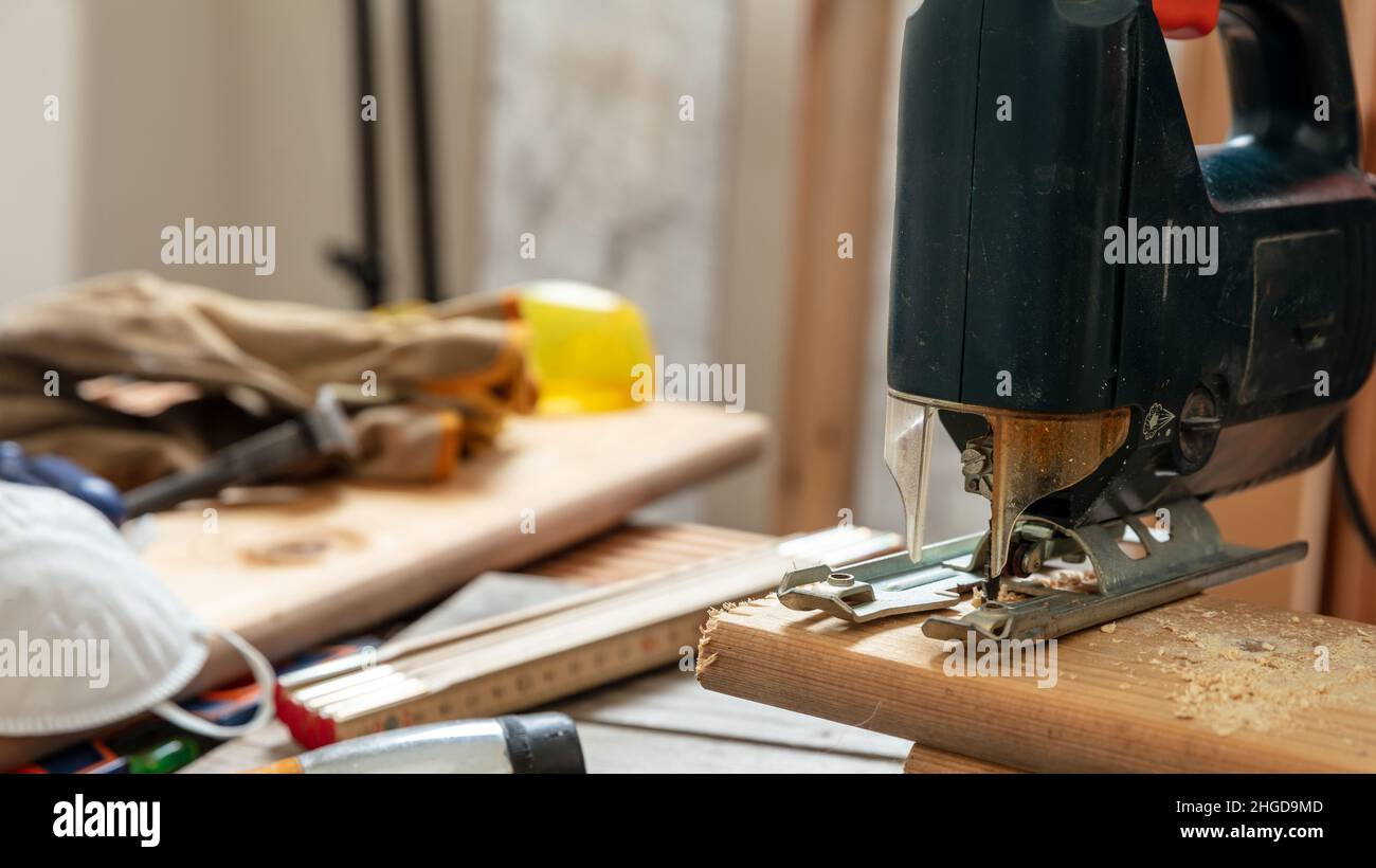 Electric jigsaw cutting wood. Construction industry, carpenter workshop, work bench table closeup view Stock Photo