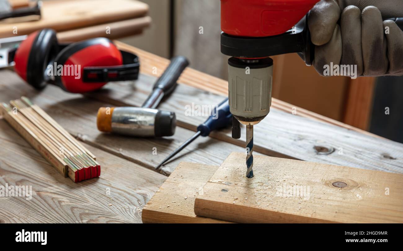 Drill electric tool, carpenter hand drilling wooden plank. Construction industry, work bench table closeup view Stock Photo