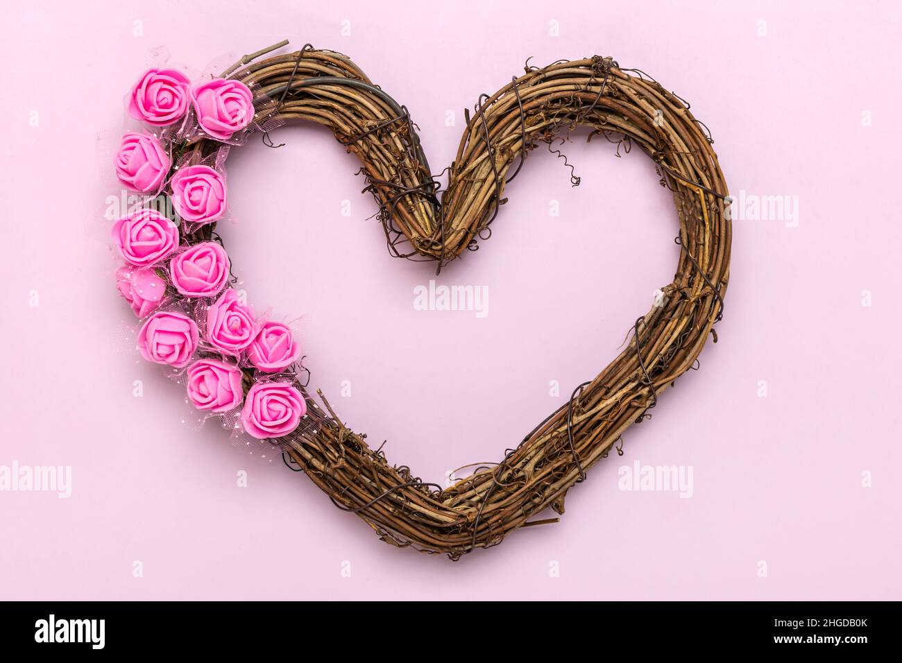 heart shaped rattan wreath decorated with flowers roses on pink background Top view Flat lay Holiday card Happy Valentine's day, love concept Copy spa Stock Photo
