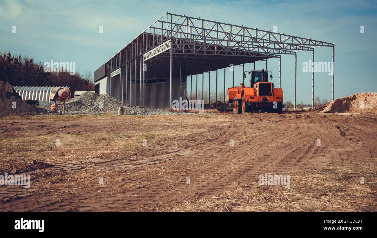 Construction of a large hangar in the countryside with the help of heavy machinery. Stock Photo