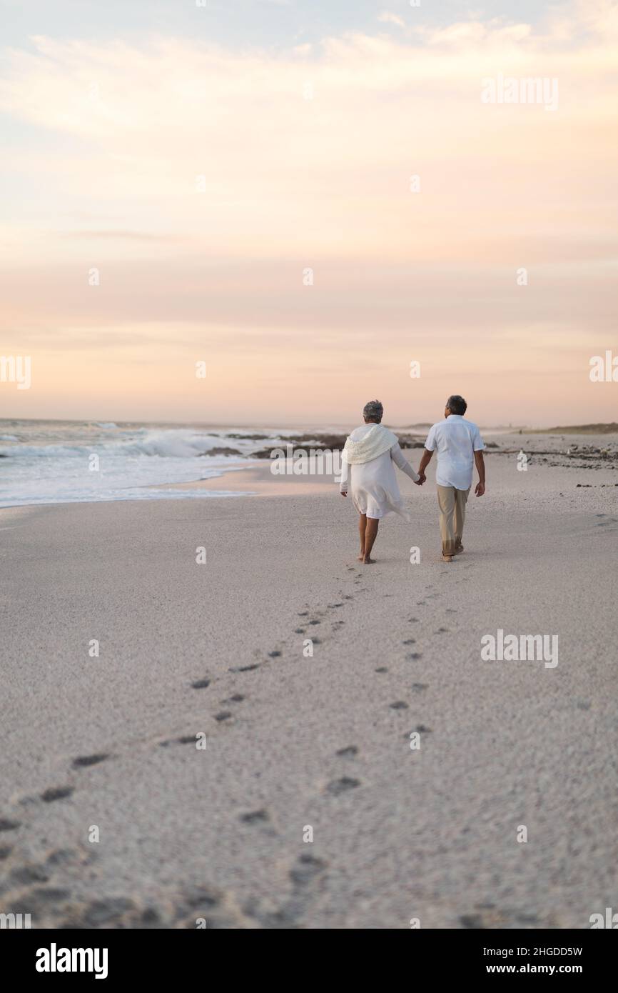 Multiracial senior couple walking while leaving footprints on sand at ...