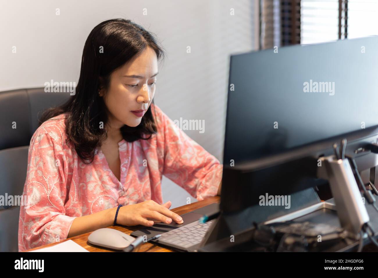 Businesswoman working on laptop sitting at her office desk with desktop ...