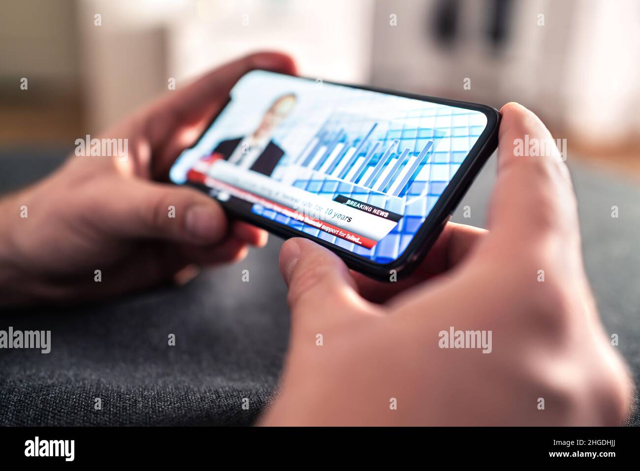 News in phone from tv broadcast stream. Man watching latest daily information from streaming live video with smartphone. Breaking headline. Stock Photo