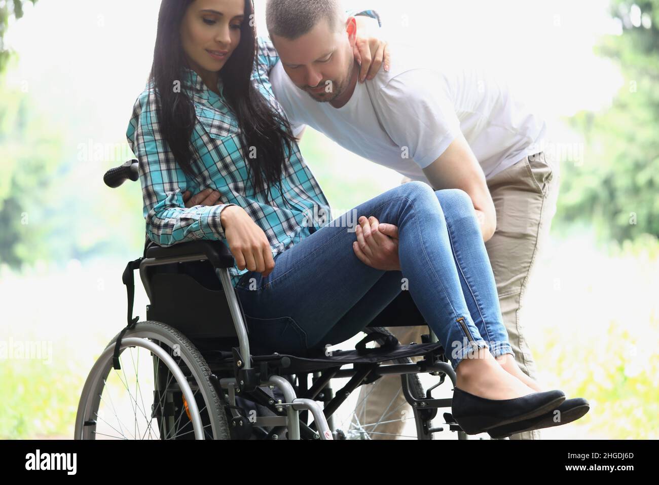 Man husband take woman in arms, disabled wife on wheelchair Stock Photo