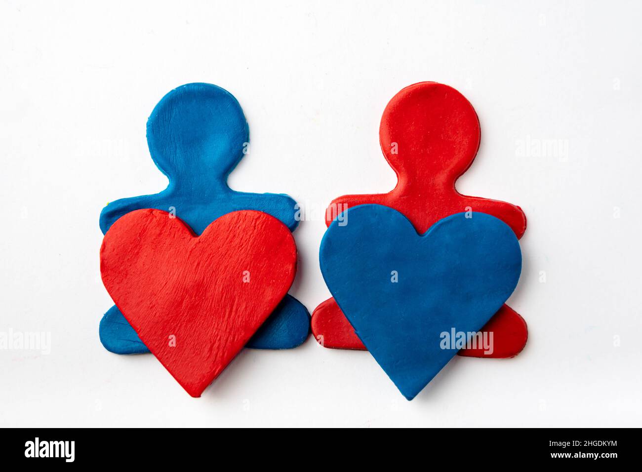 A man made of blue plasticine holds a red plasticine heart in his hands and a man made of red plasticine holds a blue plasticine heart on a white back Stock Photo