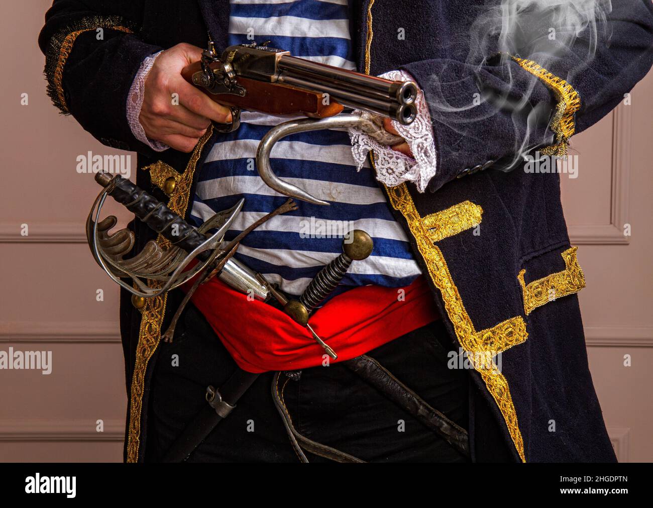 Brave armed pirate captain in a frock coat and vest with a sword and dagger and a smoking gun close-up Stock Photo