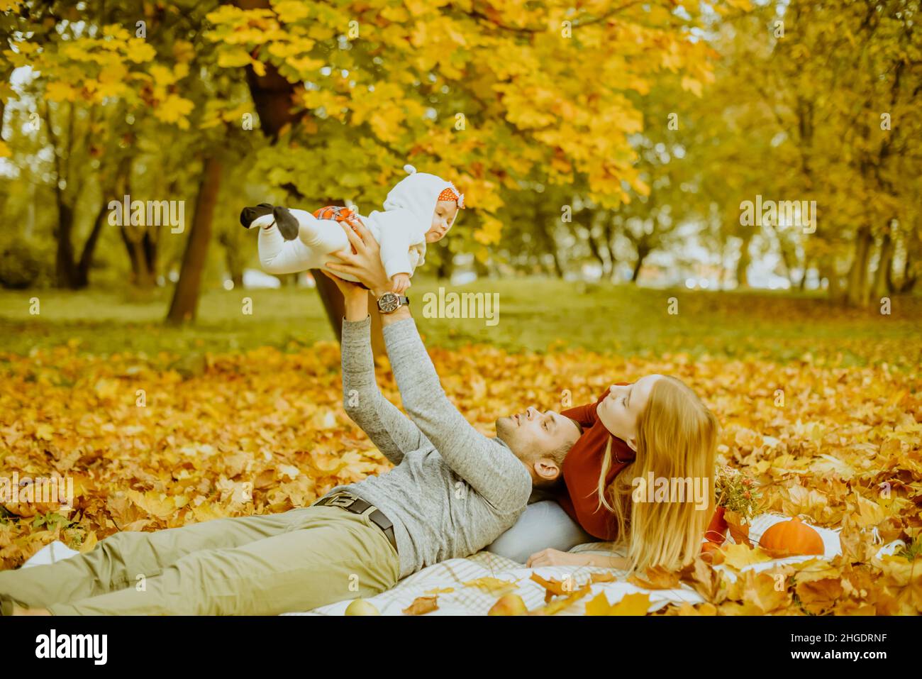 Couple in love are lying on autumn fallen leaves in a park, lying on the rug , enjoying a beautiful autumn day. Happy joyful young family father, moth Stock Photo