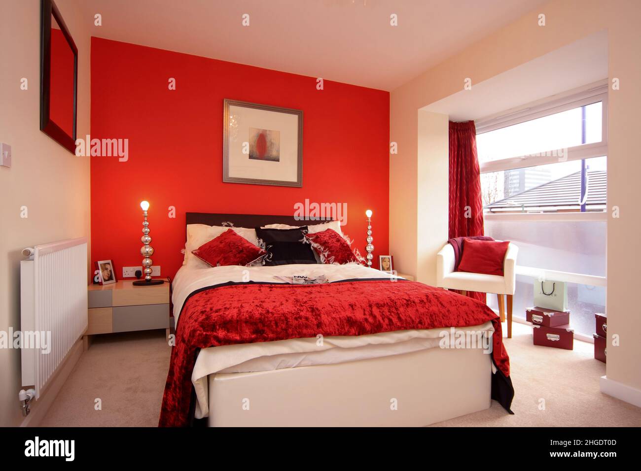 Bedroom, double kingsize bed, bright vivid red colour color scheme, velvet bedspread and cushions,bedside lights, red feature wall Stock Photo