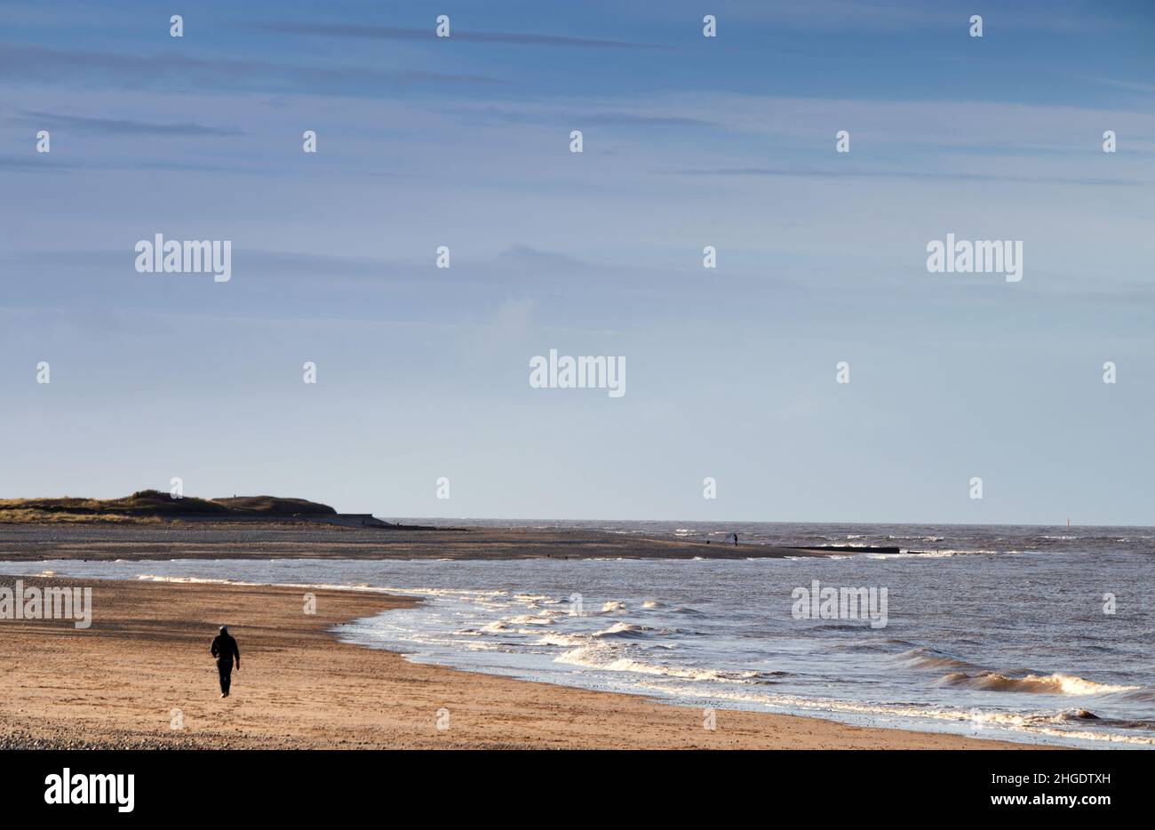 A lone figure in the foreground and a distant fisherman on the promontory of Fleetwood beach, Lancashire, Fylde Coast Stock Photo