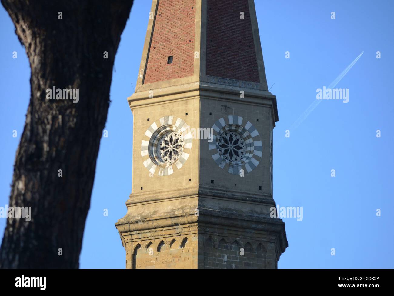 a tree trunk, a steeple and a flying airplain against blue sky. Selective focus picture Stock Photo