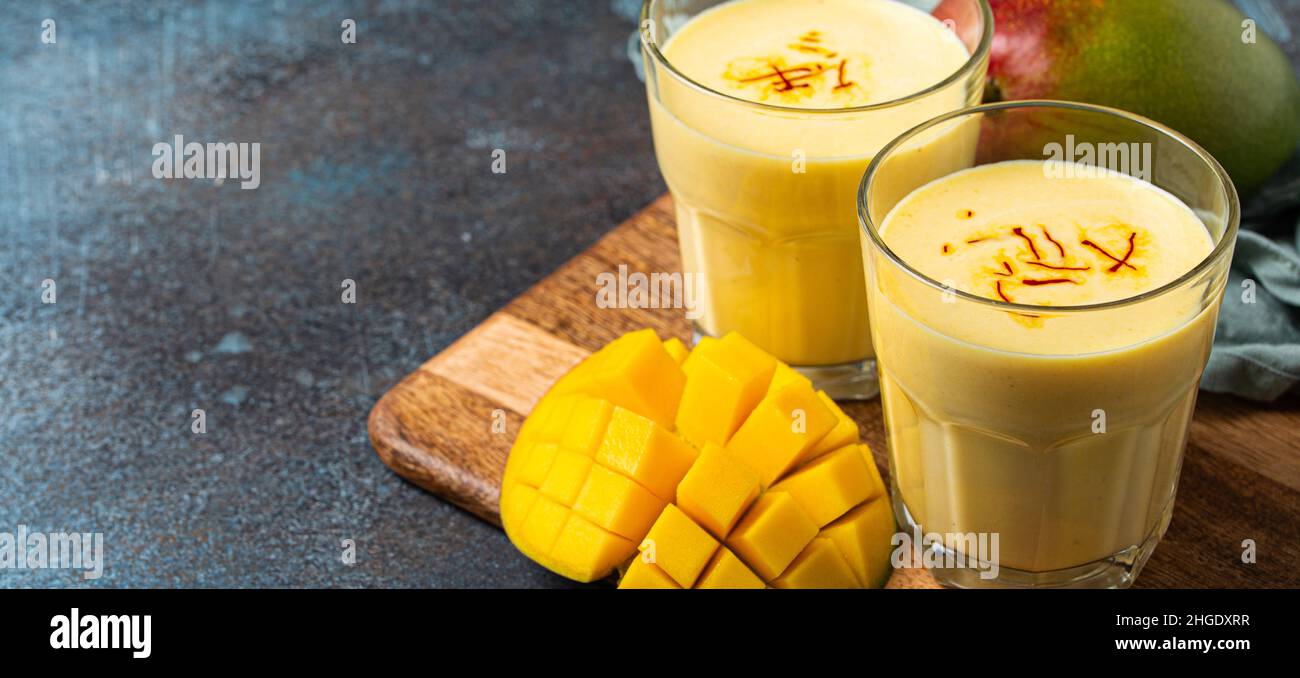 Drink mango lassi in two glasses on rustic concrete table with fresh ripe cut manfo from above Stock Photo