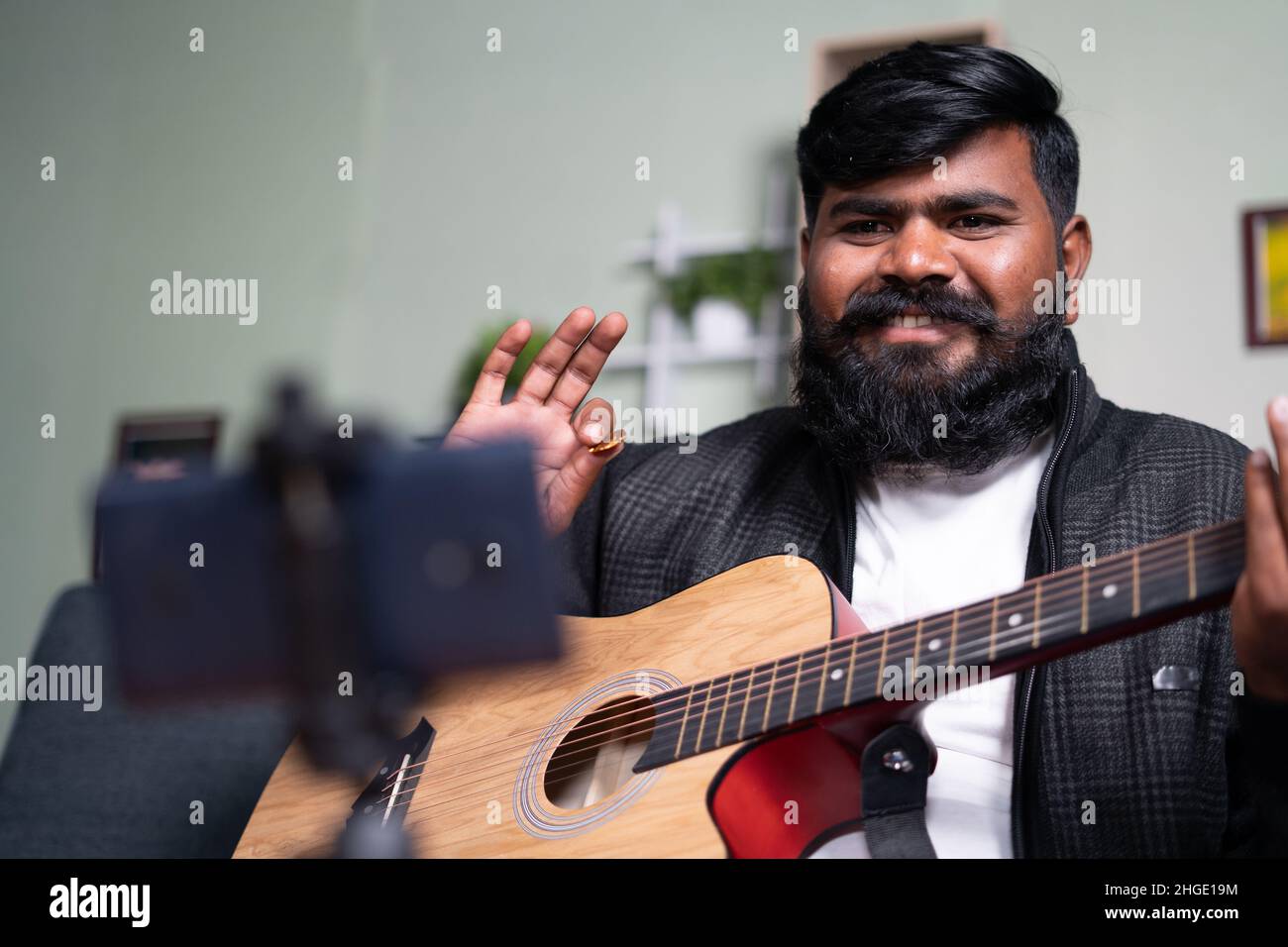 young beard mucisian learning guitar through online class by using mobile phone at home - concept of live streaming, distance teachings, vlogger and Stock Photo