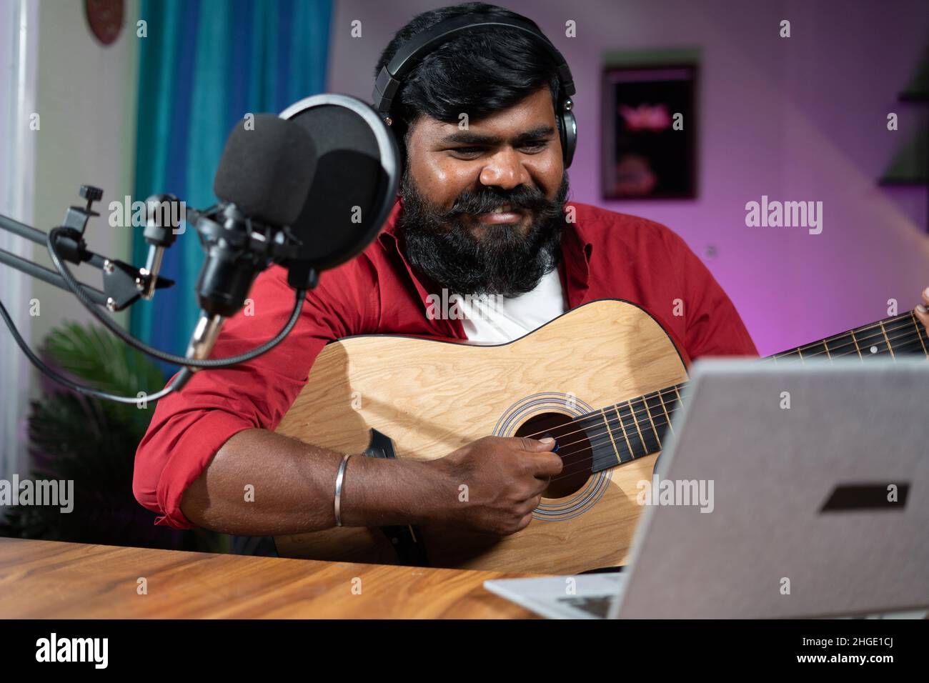 young beard mucisian teaching guitar through online class on laptop - concept of virtual training, e-learning, social media live streaming and Stock Photo