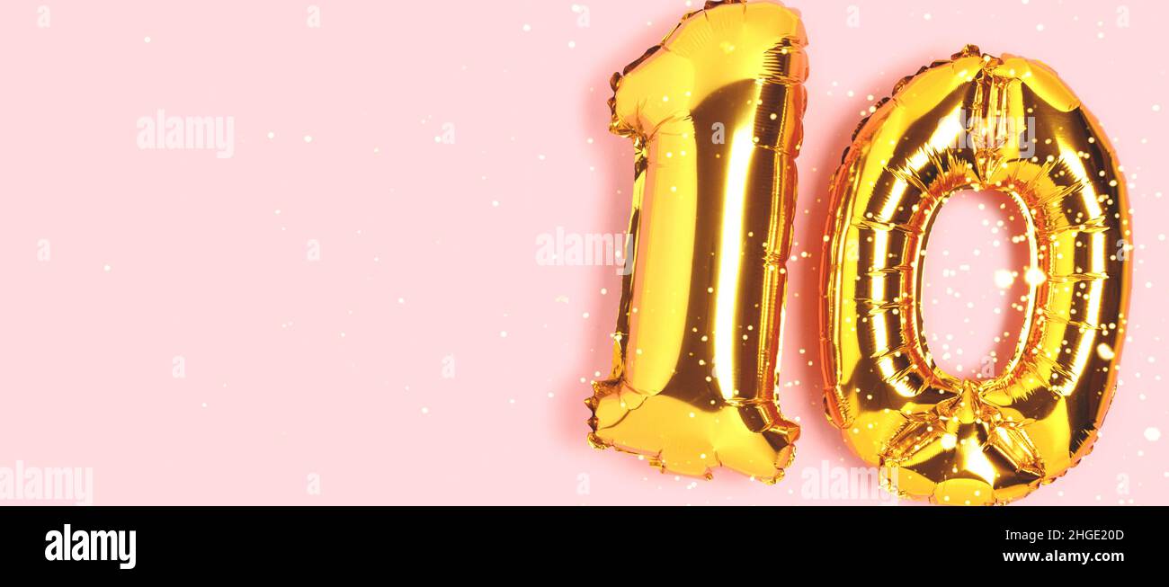 Banner with number 10 golden balloons with copy space. Ten years anniversary celebration concept on a pink background. Stock Photo