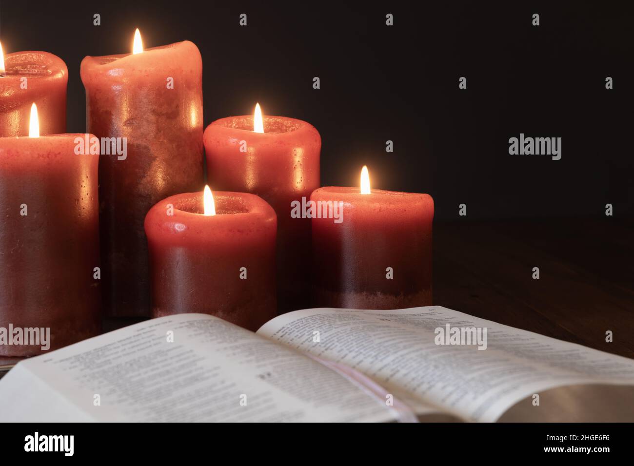 Open Christian bible and red candles burning in a dark room with copy