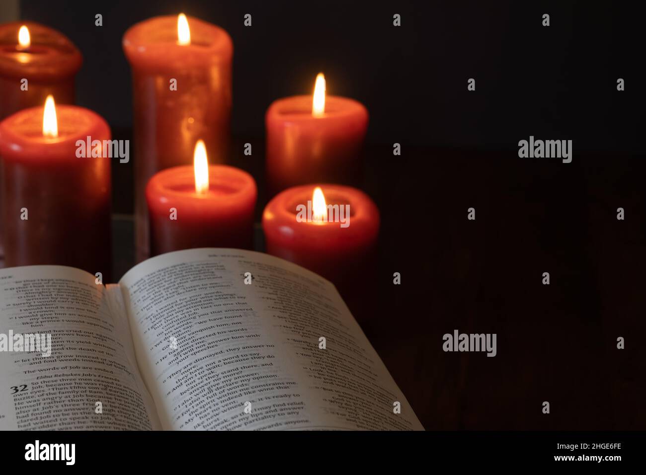 Open Christian bible and red candles burning in a dark room with copy