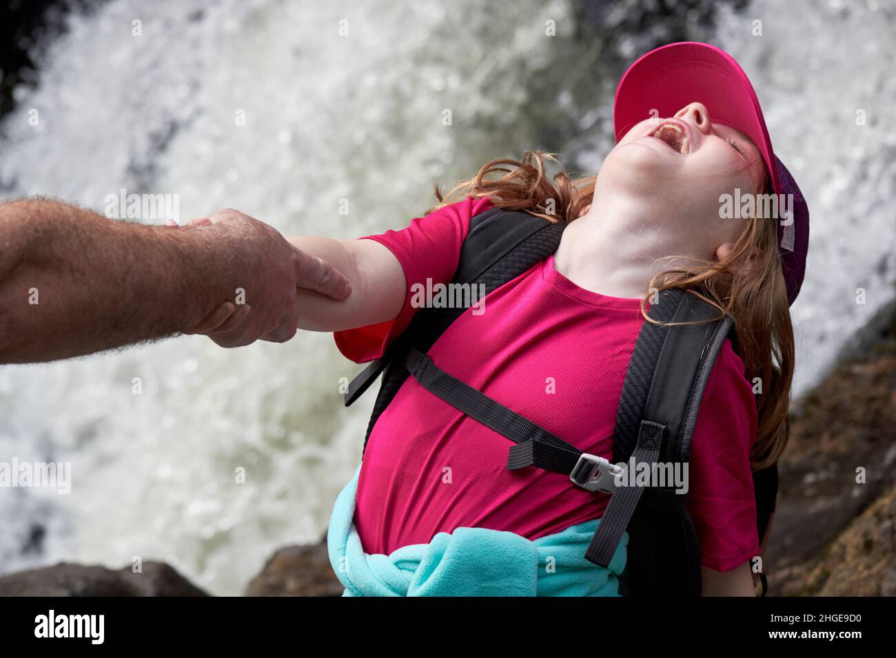 young girl pretending to fall into waterfall being held by her dads arm lake district, cumbria, england, uk Stock Photo