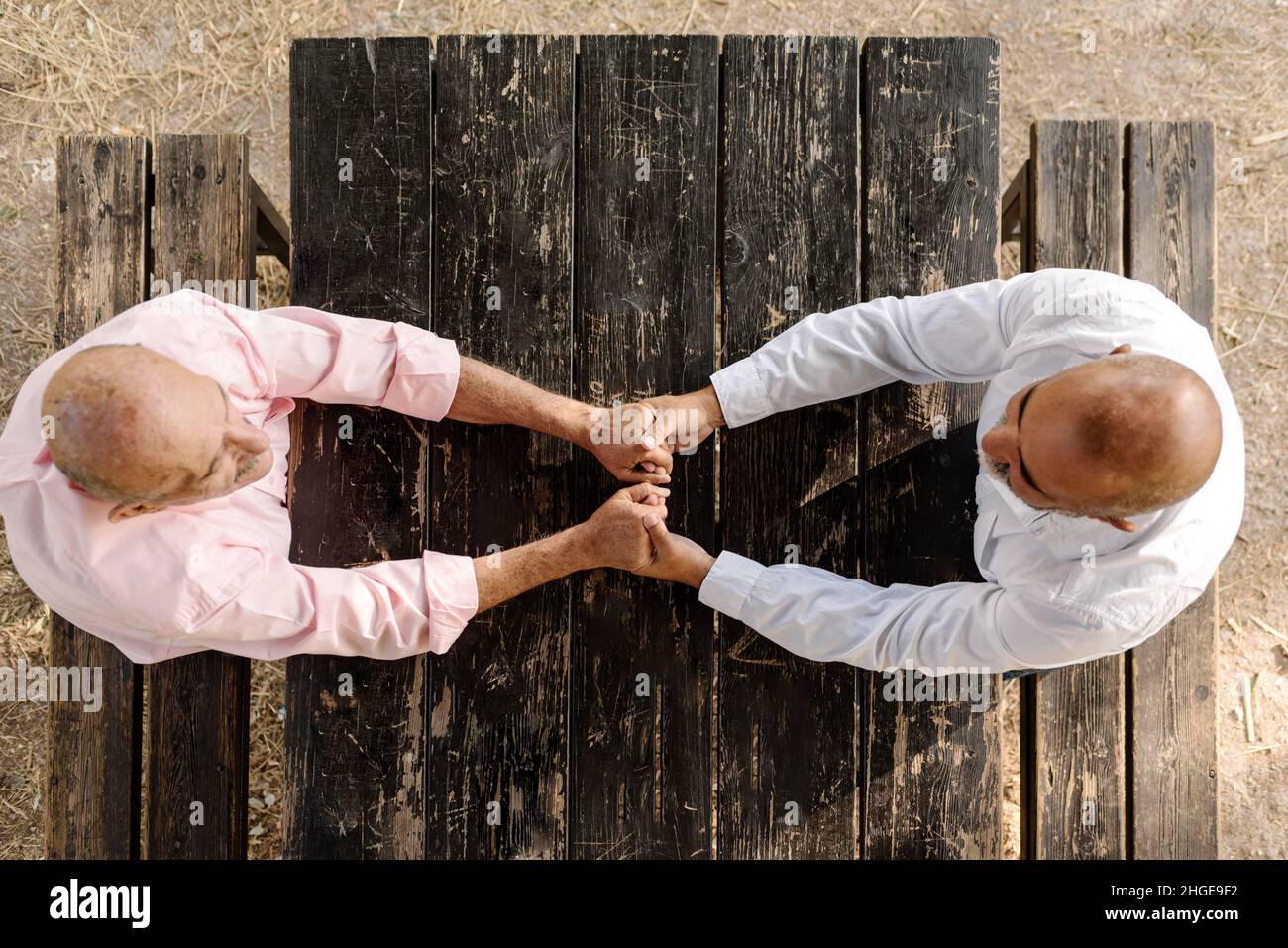 Top view of a romantic gay couple holding hands while sitting at a table in a park outdoors. Stock Photo