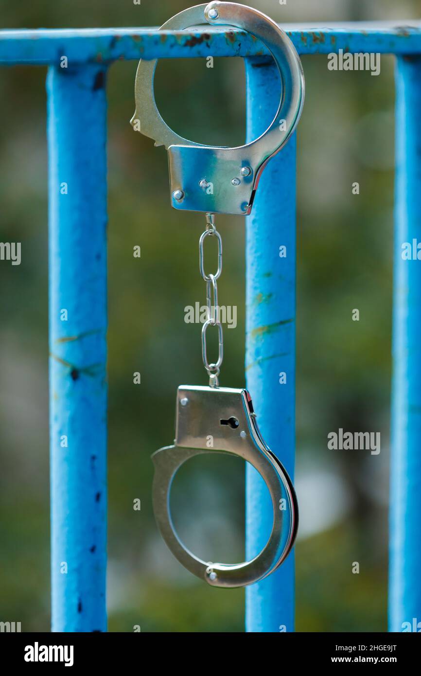 silver handcuffs hanging on a blue grate Stock Photo